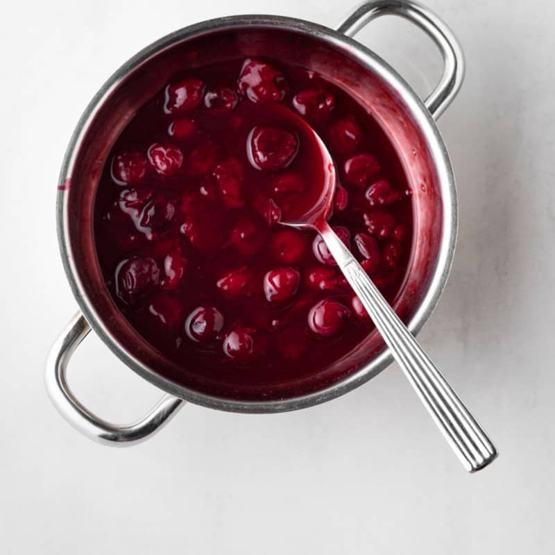 A pot filled with cherries being cooked with a spoon on top.