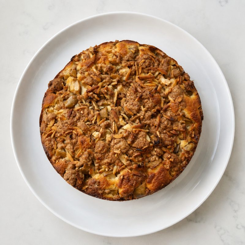A full Pear and Almond Crumble Cake on a white plate.