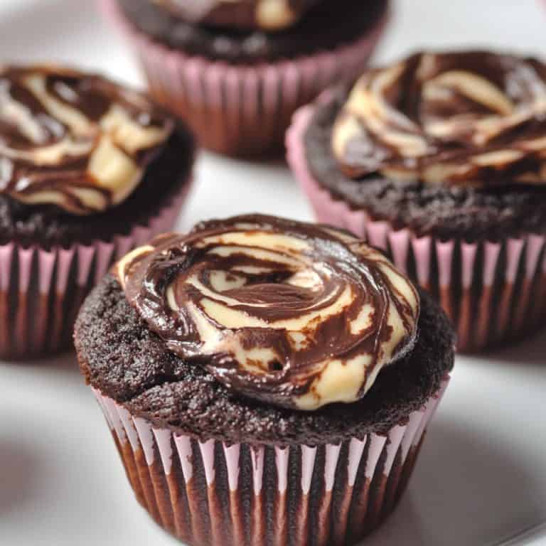 4 chocolate cheesecake muffins in pink liners on a white plate. The cheesecake has been swirled after piping.