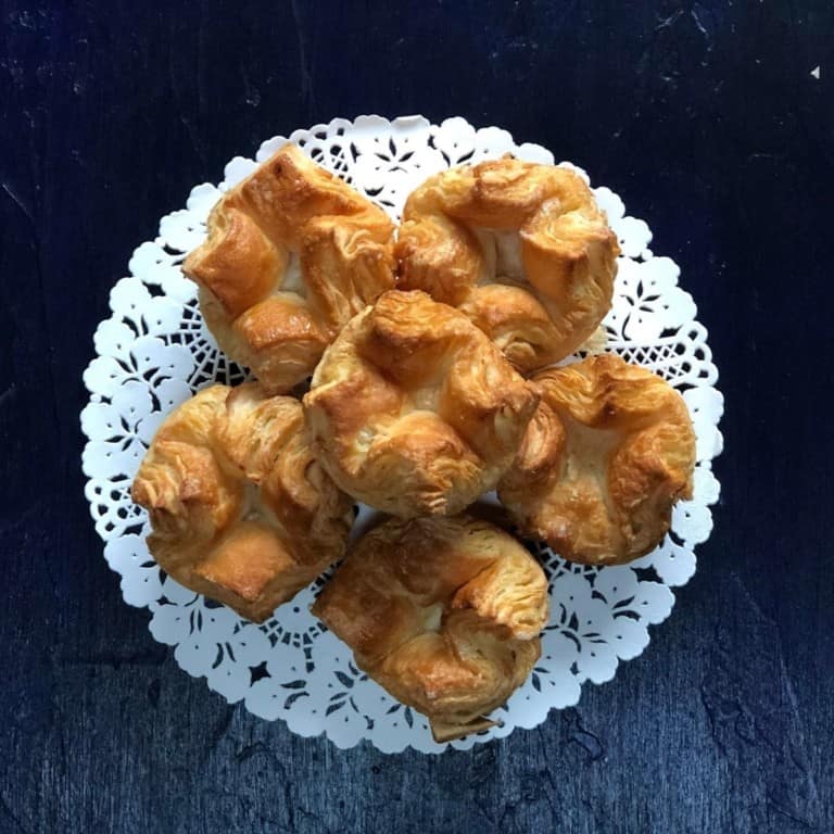Black background with a white doily with 6 Kouign Amann.