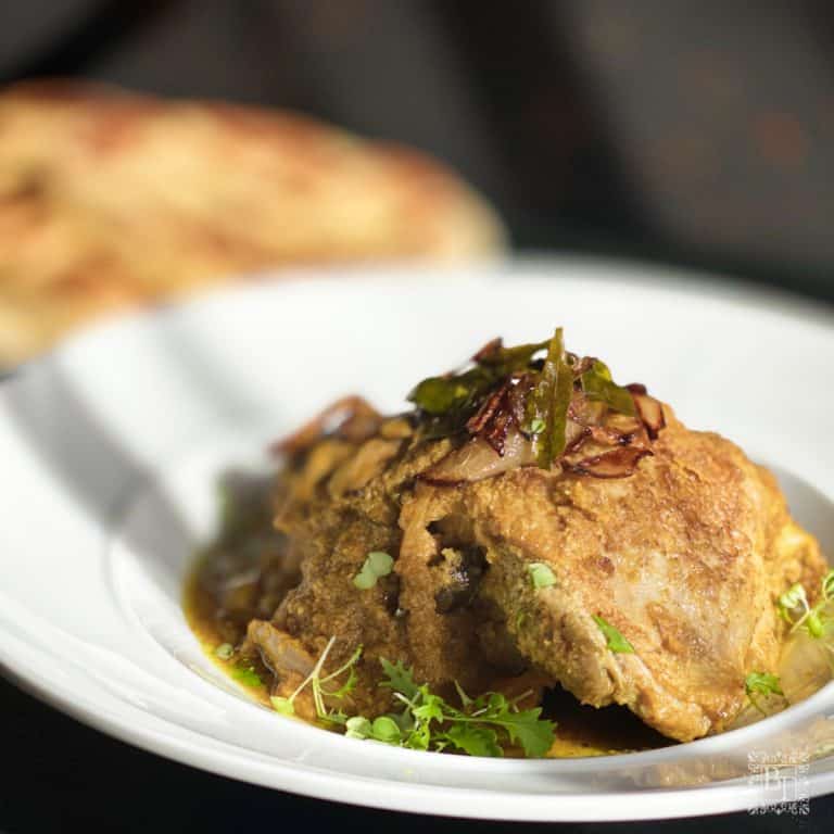 A white bowl with coconut chicken curry at the front and a plate of naan behind.