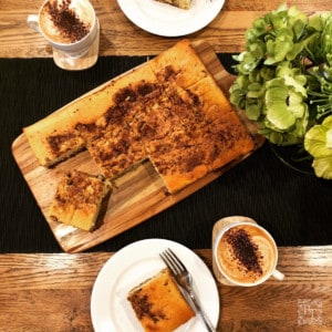 Looking down on a Coffee Tray bake on a wooden table and cups of coffee.