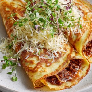 A white plate with two spanish pancakes filled with savoury mince.