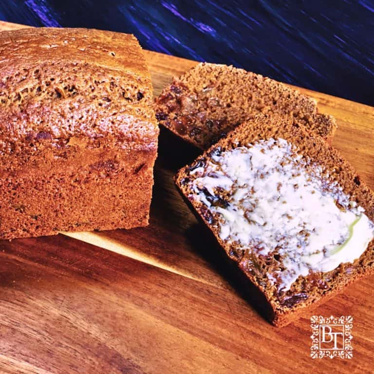 A malt loaf on a wooden board 2 slices cut off the end and one with butter spread on it.