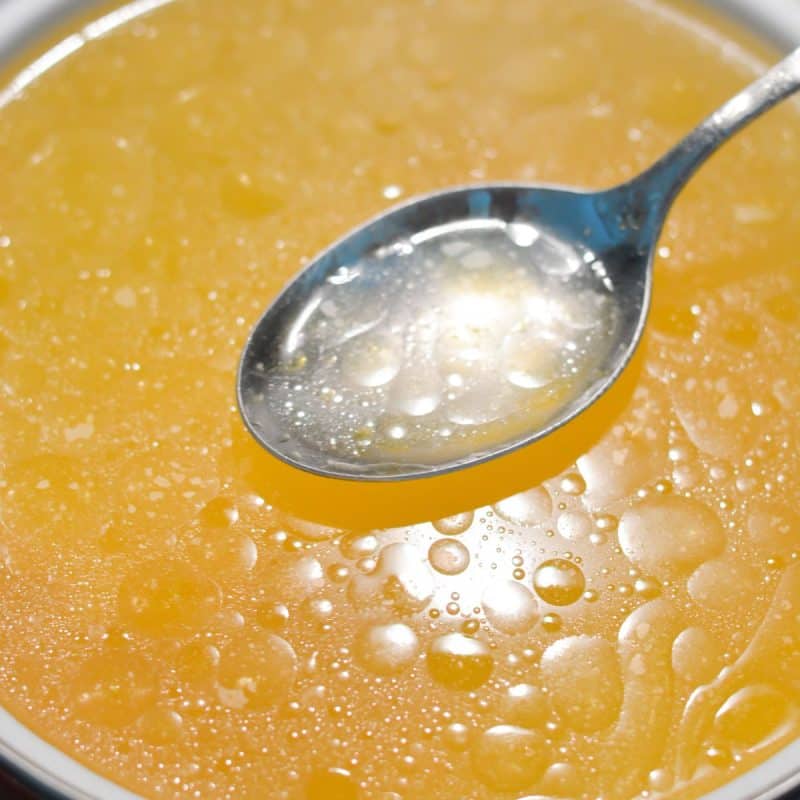 A white bowl with chicken consommé and a spoon showing the clarity.