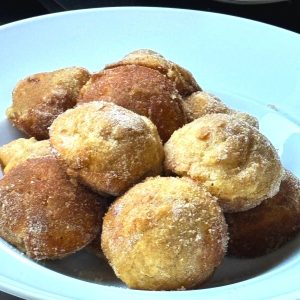 A white bowl filled with apple puffs that have been dredged in cinnamon sugar.