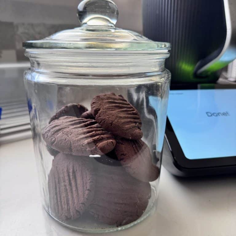 A glass jar filled with homemade chocolate ripple biscuits, all sitting in front of a Thermomix TM7.