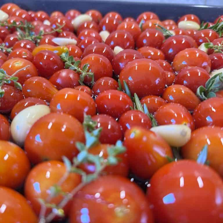 a large tray of tomatoes with cloves of garlic herbs and oil drizzled over them.